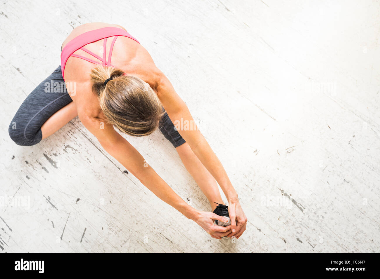 Woman sitting on wooden floor stretching leg Stock Photo - Alamy
