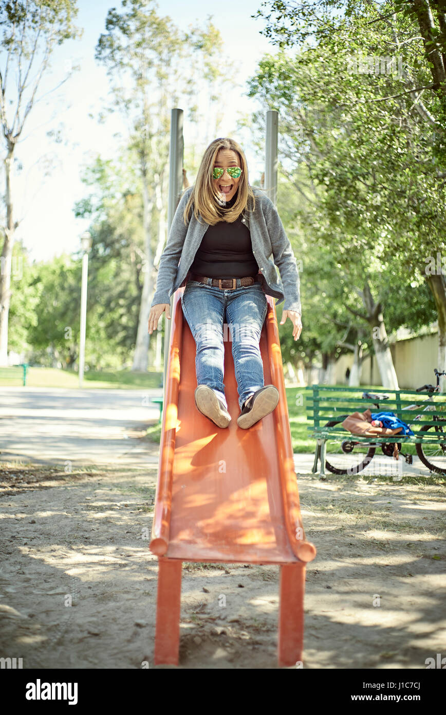 Hispanic woman on slide at playground Stock Photo