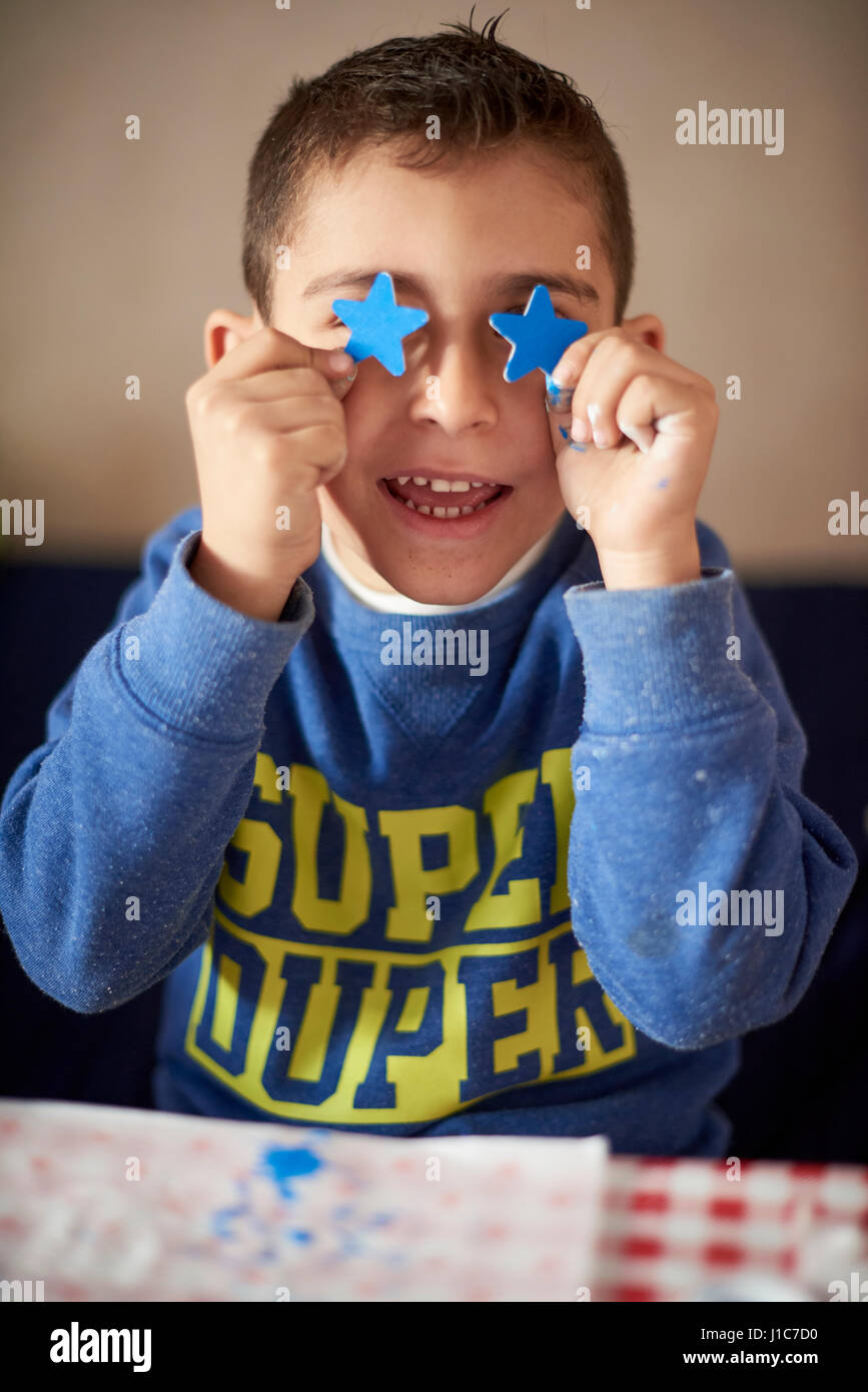 Hispanic boy covering eyes with blue stars at table Stock Photo