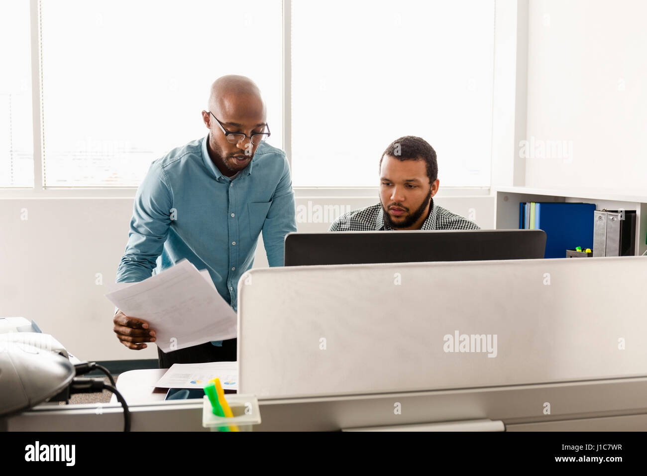 Men working at computer with paperwork in office Stock Photo