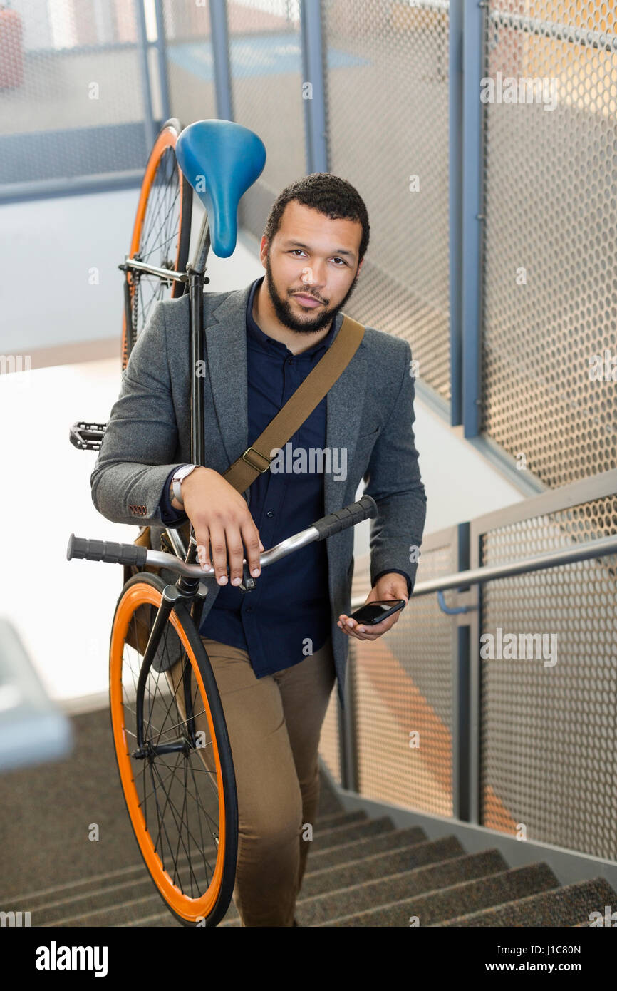 Mixed Race man climbing staircase carrying bicycle Stock Photo