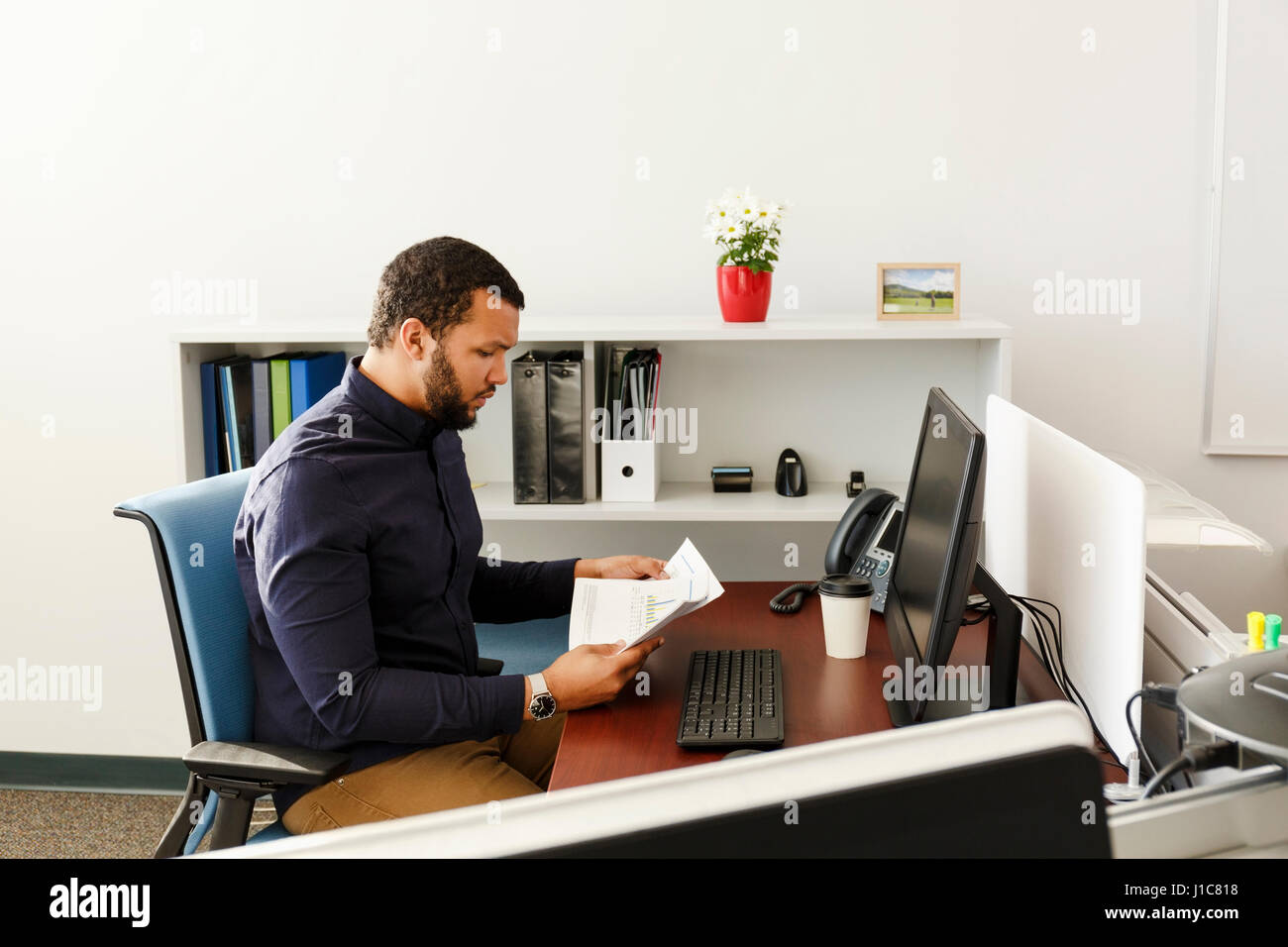 Mixed Race man reading paperwork near computer in office Stock Photo