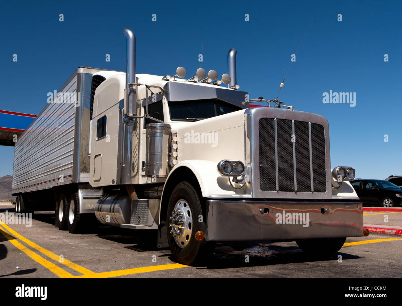 White color classic custom build and designed big rig semi truck with reefer trailer with chrome accents standing in the lined parking lot Stock Photo