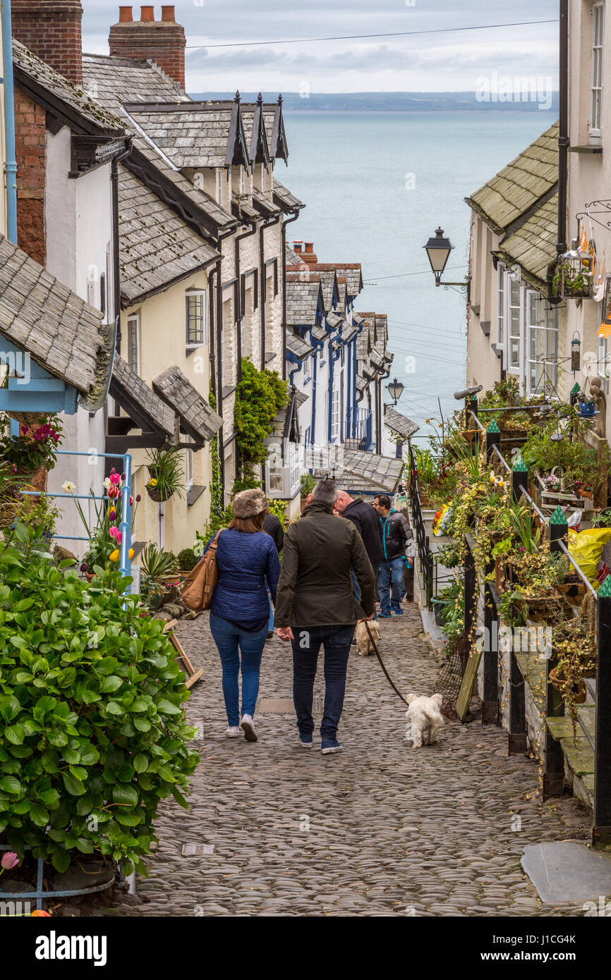 Clovelly, North Devon,England,UK. A couple walking a dog enjoy the  picturesque cottages, and steep cobbled high street of this secluded Devon village Stock Photo