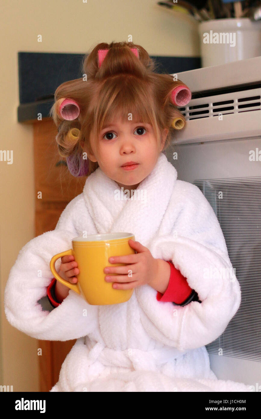 little blonde haired girl in hair curlers and robe drinking her morning