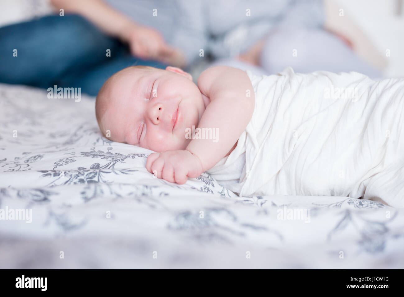 Young parents resting in bed, their newborn daughter sleeping in th e foreground. Stock Photo
