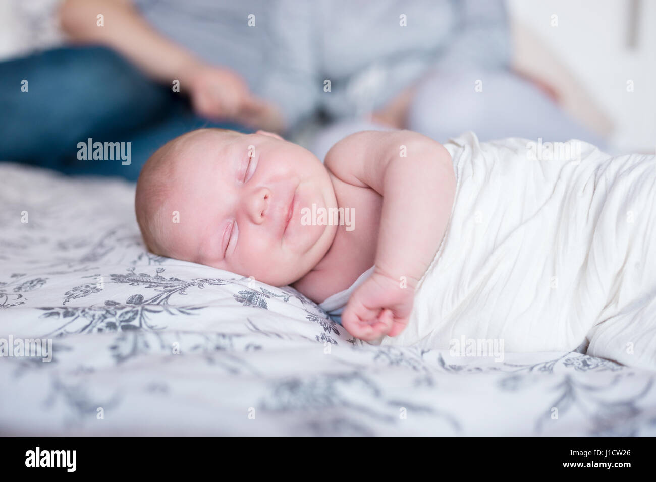 Young parents resting in bed, their newborn daughter sleeping in th e foreground. Stock Photo