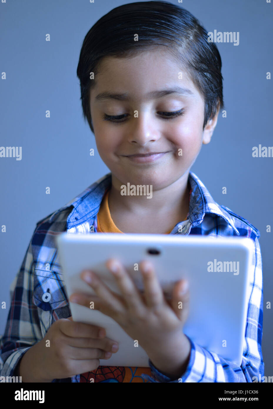 Kid with tablet computer. Child thinking holding tablet. Smiling kid with digital technology looking at the tablet. Stock Photo