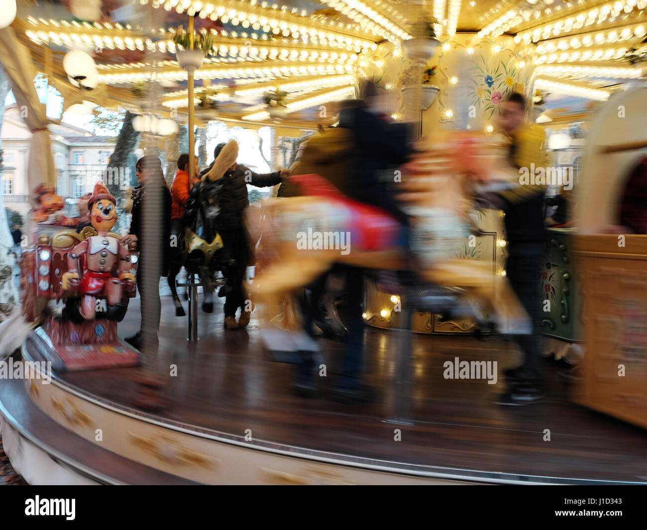 Moving Carousel - Pinocchio - Merry-go-round spinning around, woman wearing sunglasses freezed in colorful background - Lucca, Tuscany, Italy, Europe Stock Photo