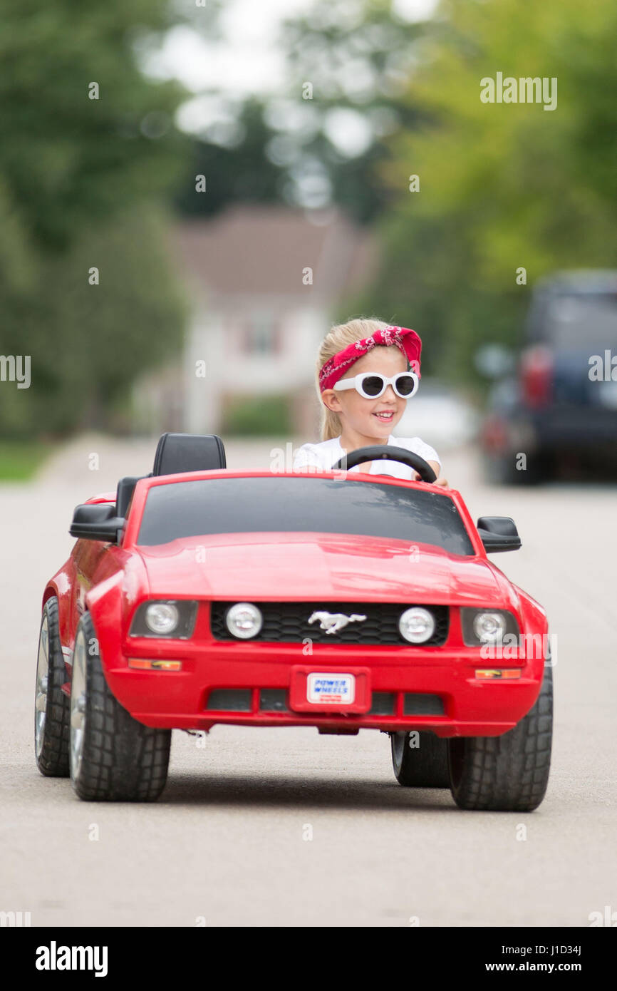 4 year old blonde girl driving red mustang with white sunglasses and red  bandana Stock Photo - Alamy