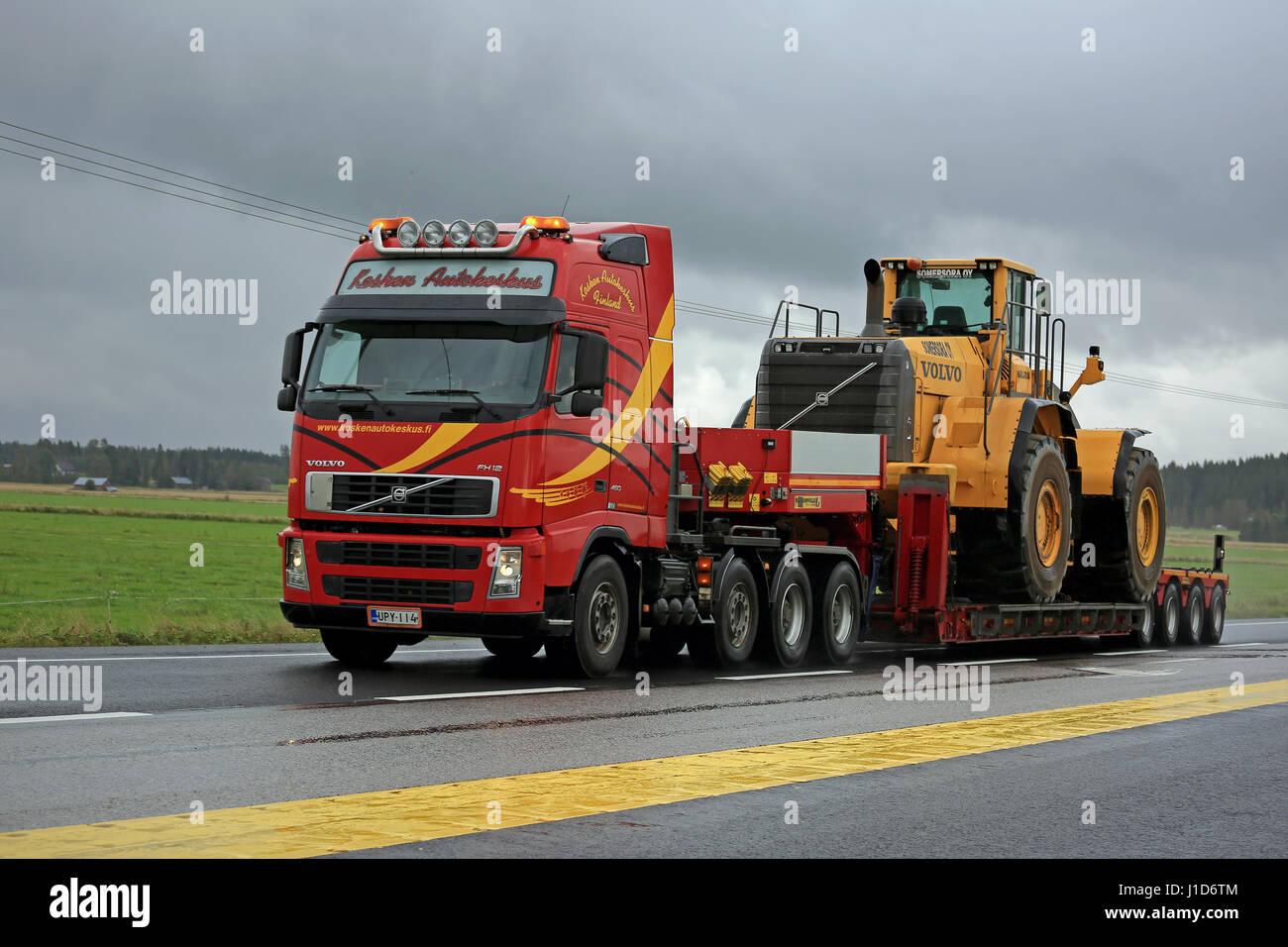 FORSSA, FINLAND - SEPTEMBER 4, 2016: Red Volvo FH12 semi truck transports Volvo wheel loader as oversize load along highway on a rainy day. Stock Photo