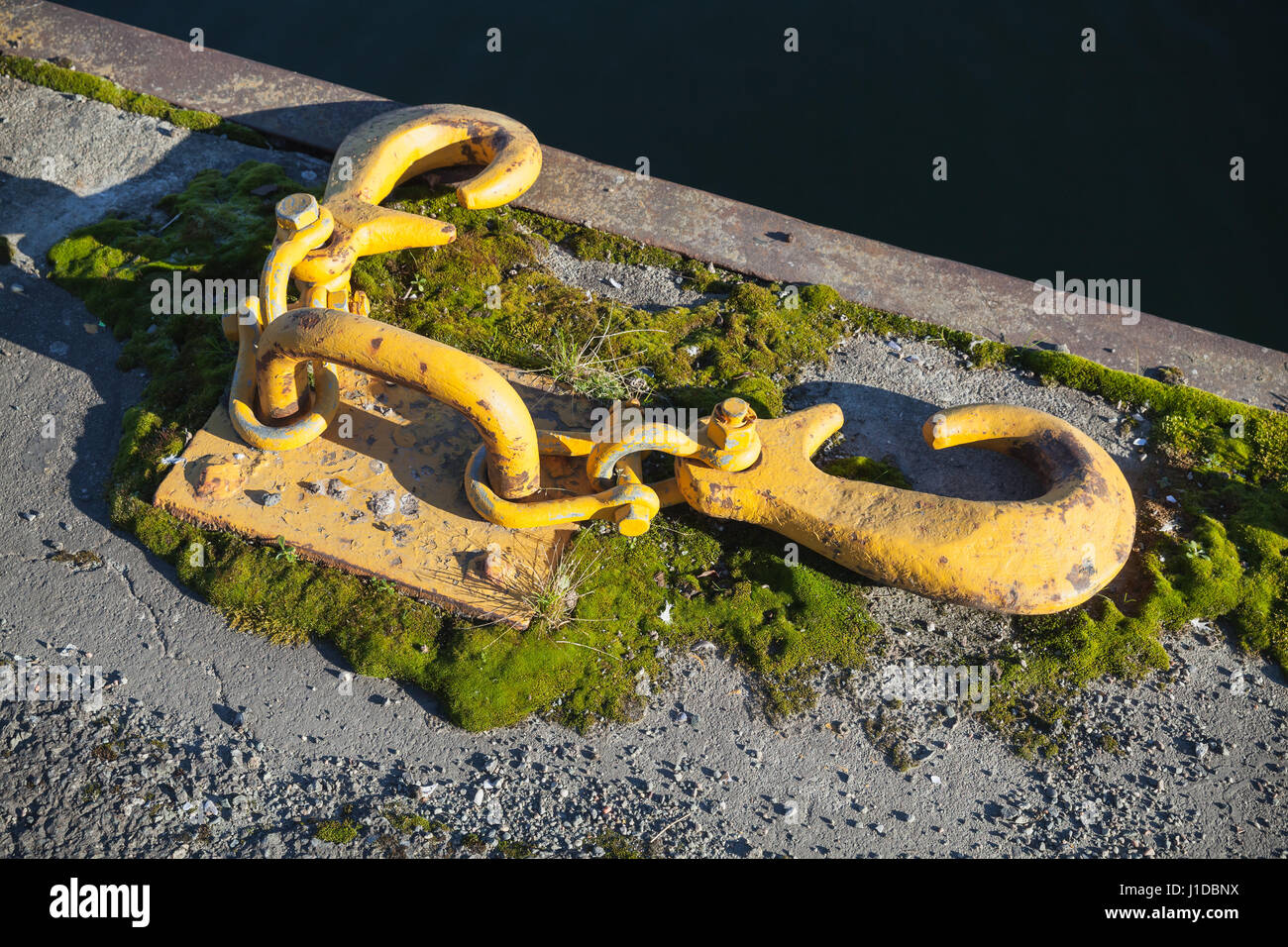 Ships mooring equipment, yellow hooks for ropes mounted in concrete pier Stock Photo