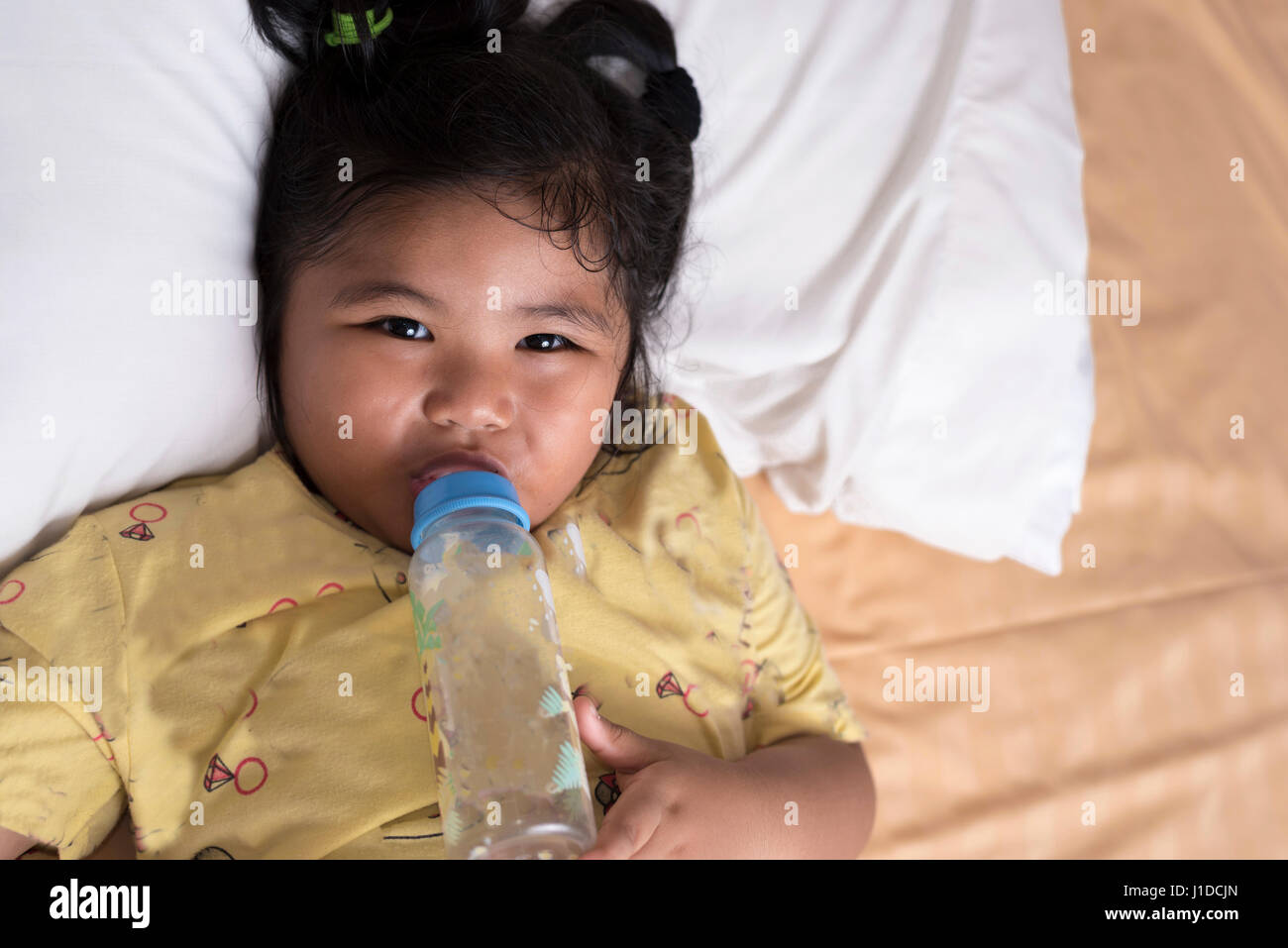 Adorable baby girl holding milk bottle and drinking on the bed in