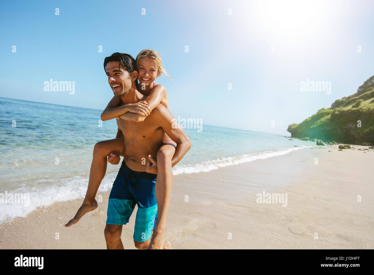 Portrait of loving couple piggyback together on tropical beach. Man carrying girlfriend on his back along the sea shore. Enjoying summer vacation. Stock Photo