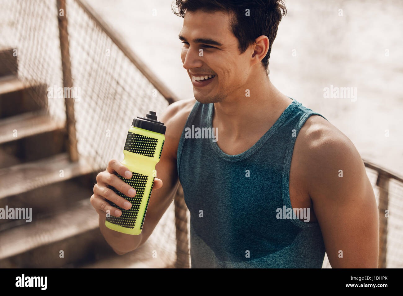Athlete resting after running with bottle of water. Rest after a hard workout at beach. Stock Photo