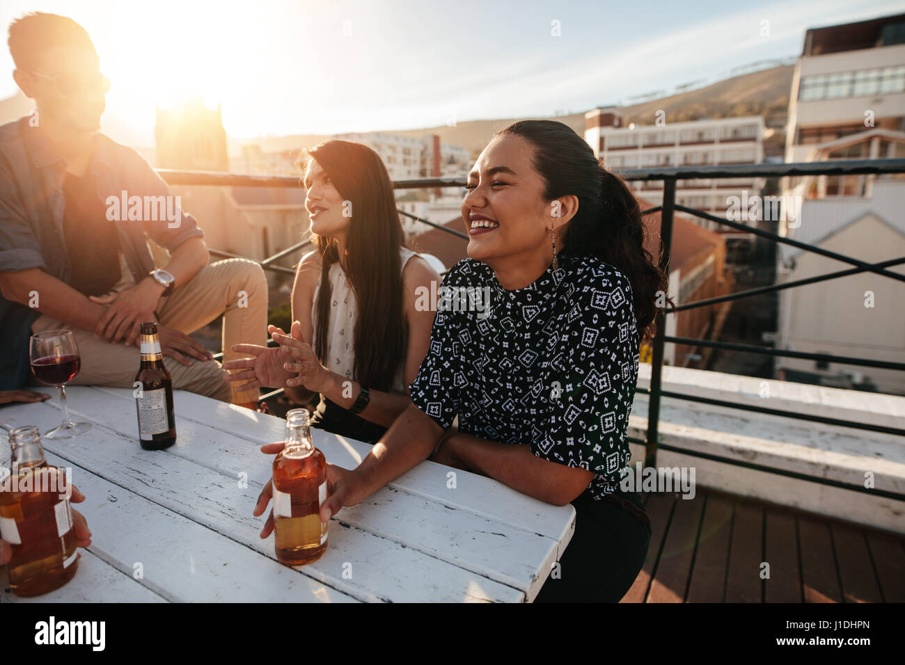 Smiling young woman having a rooftop party with friends. Friends party gathering on rooftop. Stock Photo