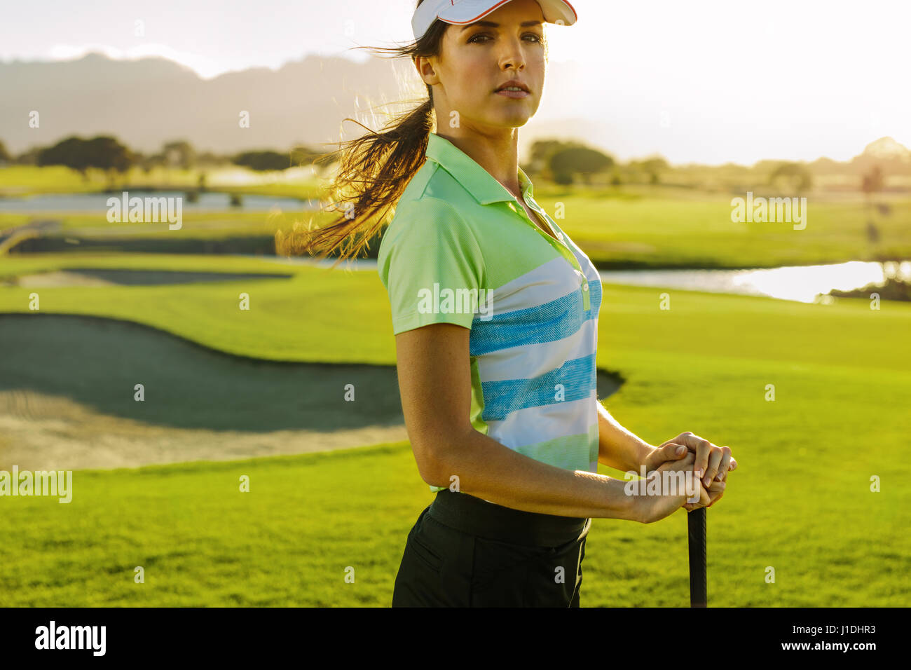 Portrait of young female golfer with golf club standing on field. Beautiful young woman on golf course on summer day. Stock Photo