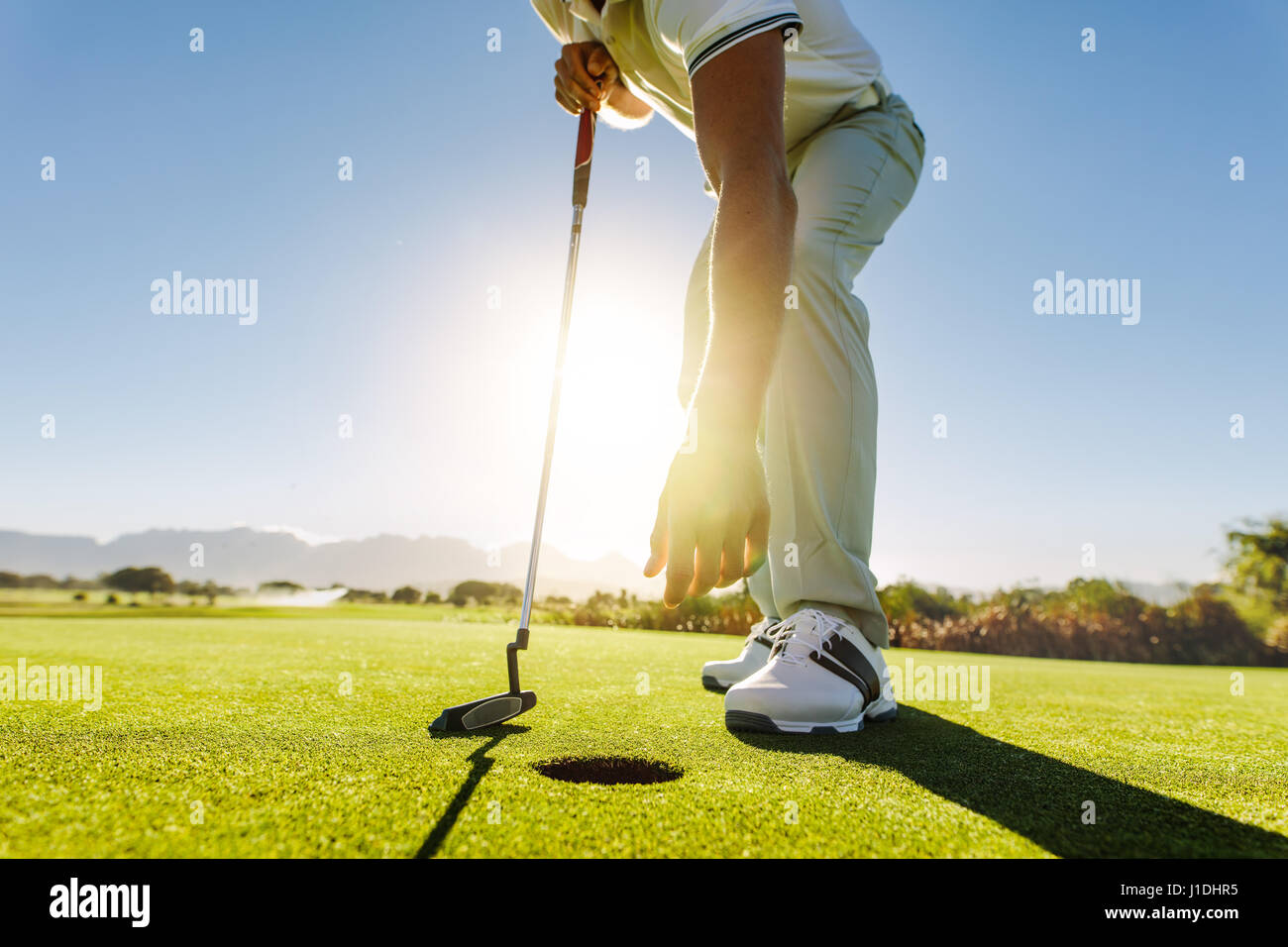 Shot of a golf player taking out the ball from hole. Golfer picking the ball from hole after successful put Stock Photo