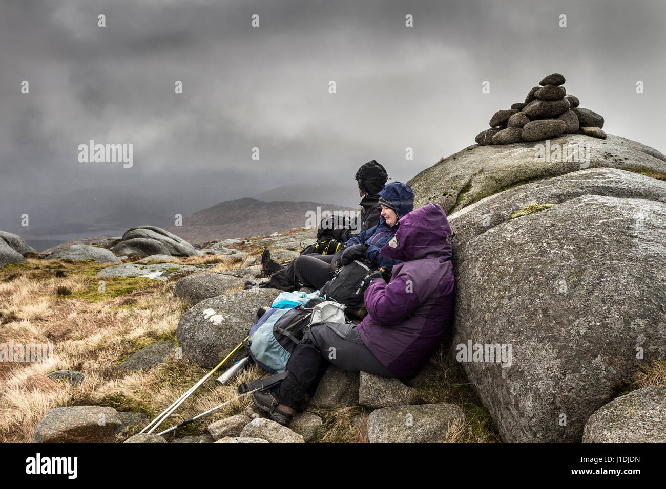 Walkers on the Summit of Criagnaw Sheltering Against the Wind as a Heavy Snow Squall Hits Them, Galloway Hills, Scotland Stock Photo