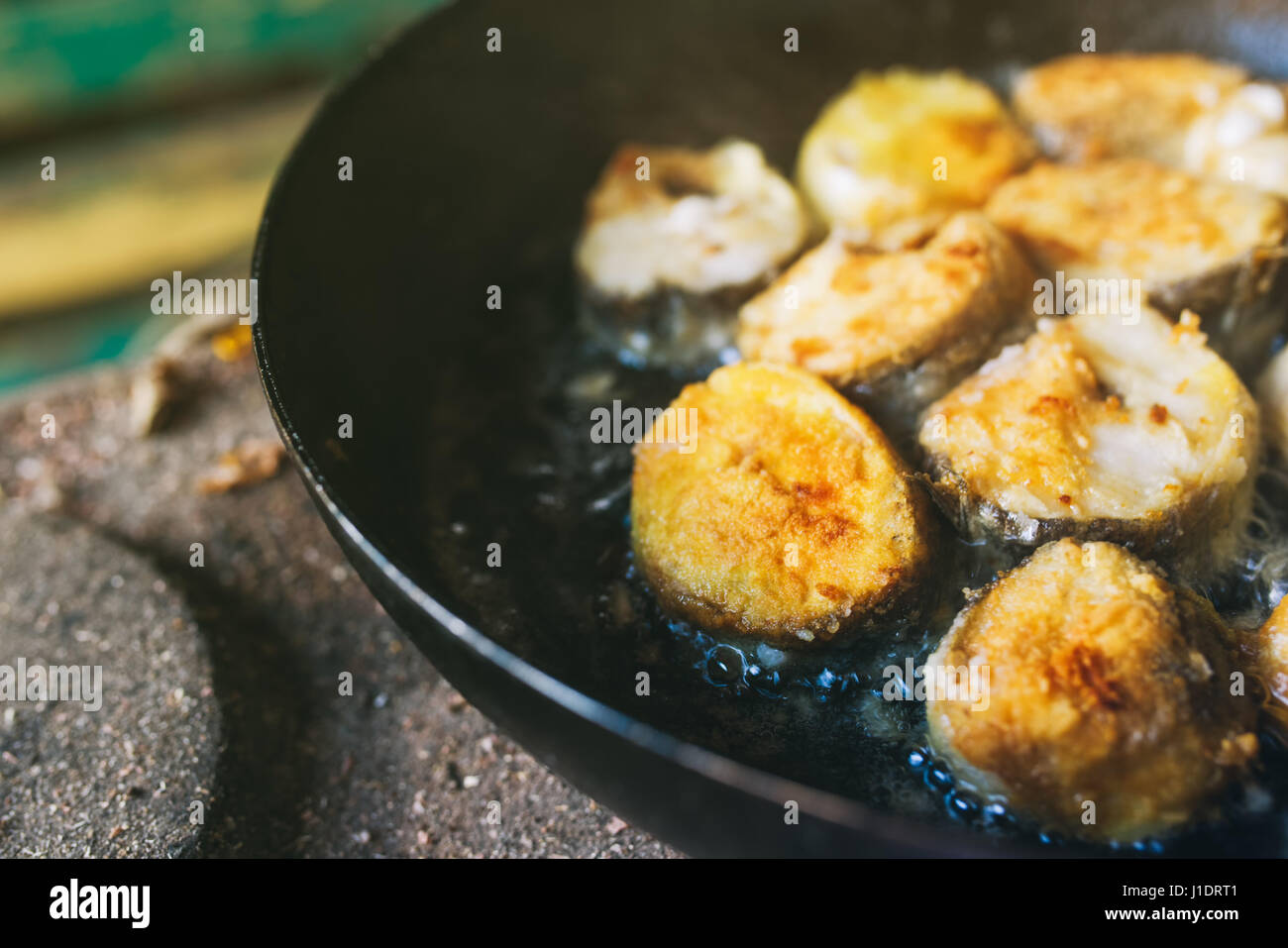 Frying hake fish outdoors on picnic, close up of frying pan with oil and fish slices Stock Photo