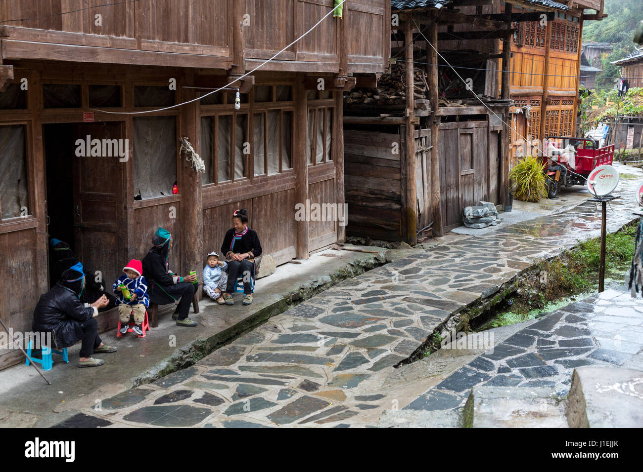 Huanggang, Guizhou, China.  A Dong Ethnic Village.  Women and Children Sitting in front of a House.  Satellite Dish on Right. Stock Photo