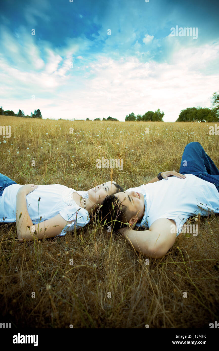 A shot of an asian couple in love lying down on grass under the blue ...