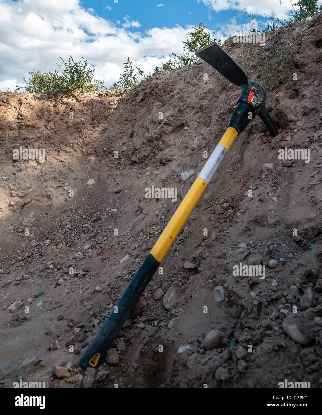A pick axe leans against the dirt in a large pit. Stock Photo