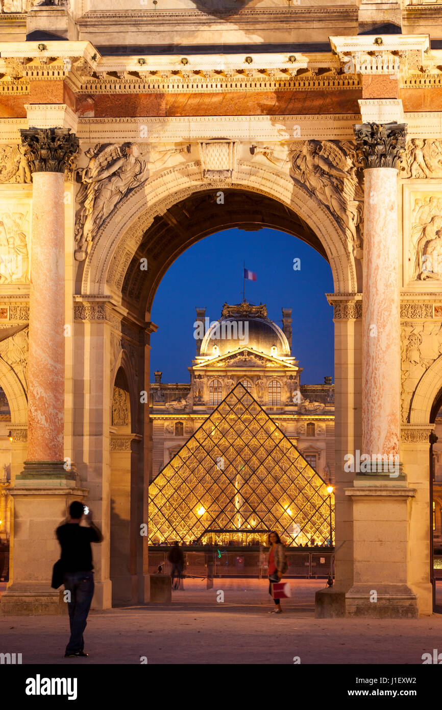 Tourists taking photos at Arc de Triomphe du Carrousel with Musee du Louvre beyond, Paris, France Stock Photo