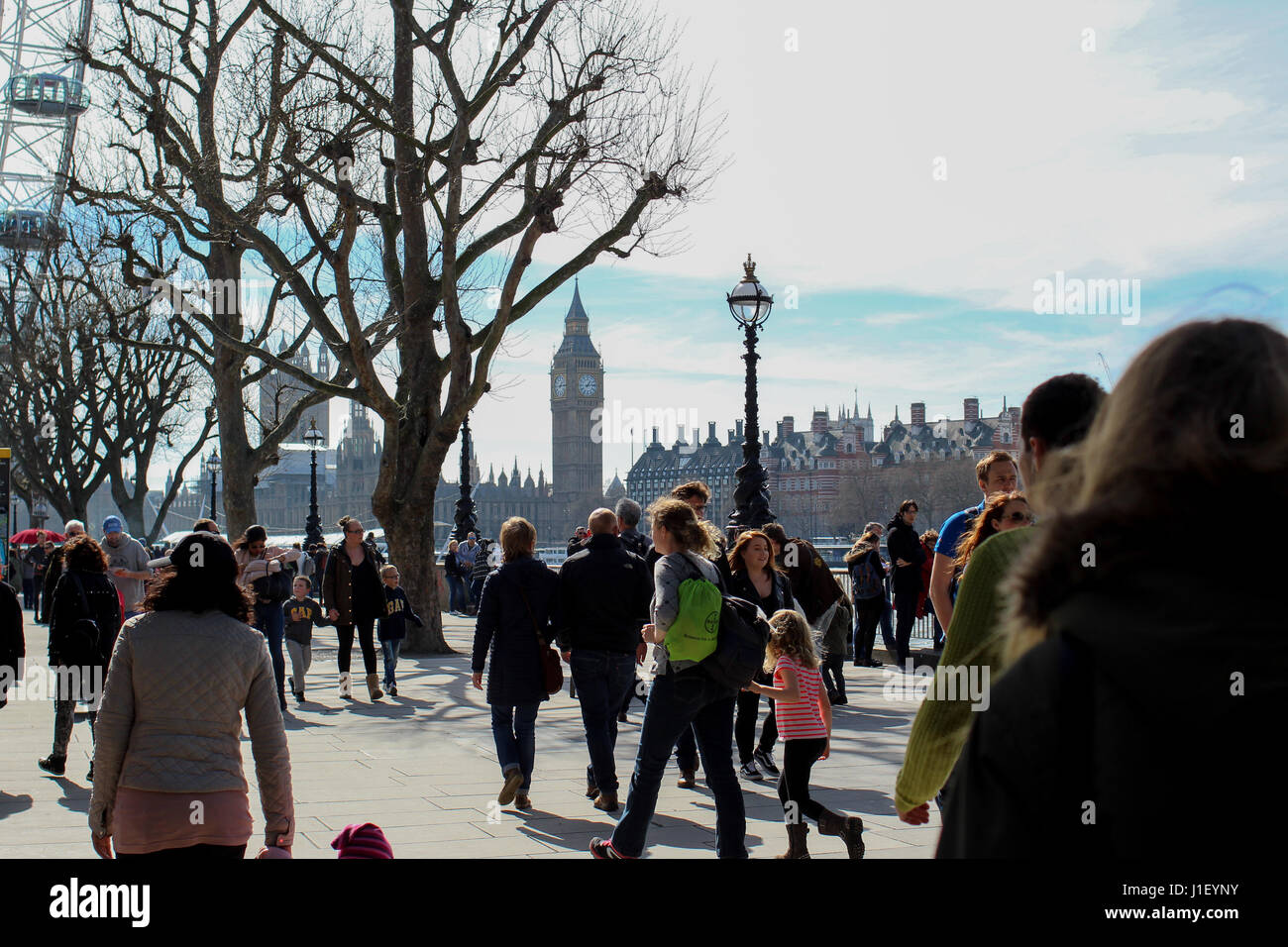 Big Ben visible in the background as crowds walk along South Bank in London on a sunny but cold spring day - blue skies and clouds Stock Photo