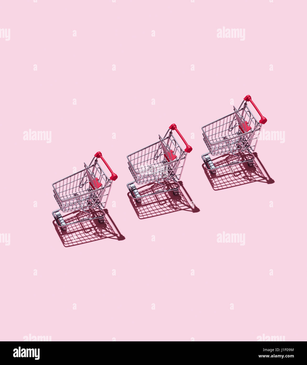 Three Shopping Carts over pink background Stock Photo - Alamy