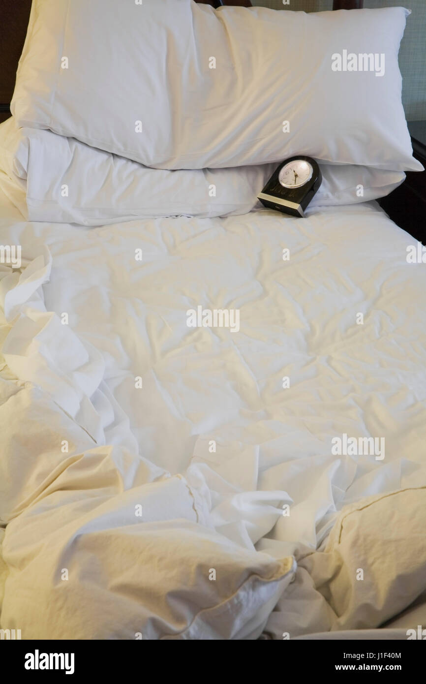 Empty bed in hotel room with wrinkled sheets and alarm clock showing