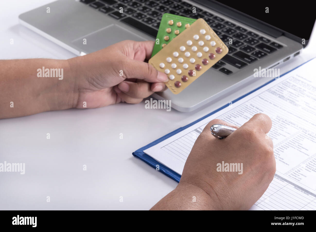 doctor hand holding birth control pills and pen over computer and patient history form on white table, healthcare, pharmacy and medicine concept Stock Photo