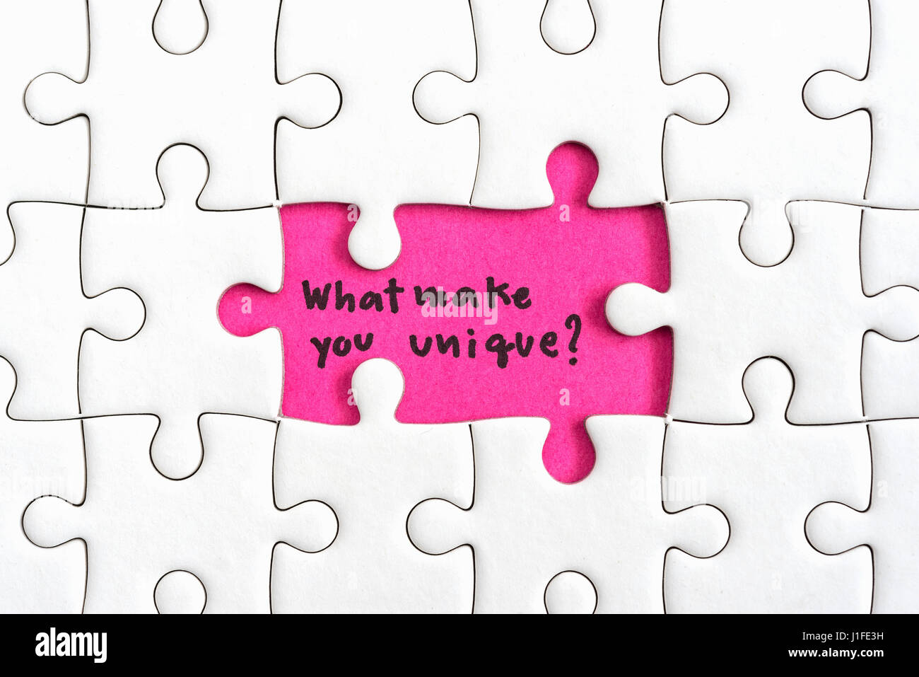 Jigsaw puzzle piece with two missing and hand writing letters word what make you unique and question mark, Quotes business concept Stock Photo