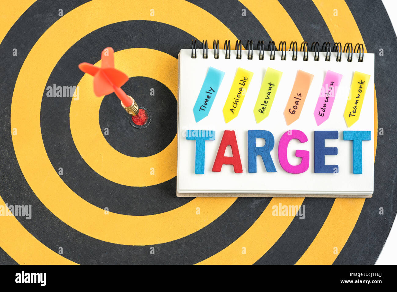 dart target in bullseye with words target on the notebook with handwriting timely achievable relevant goals education teamwork over dartboard backgrou Stock Photo