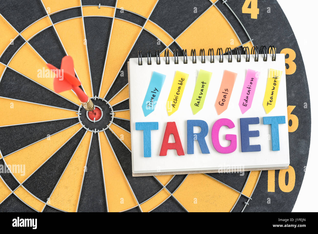 dart target in bullseye with words target on the notebook with handwriting timely achievable relevant goals education teamwork over dartboard backgrou Stock Photo
