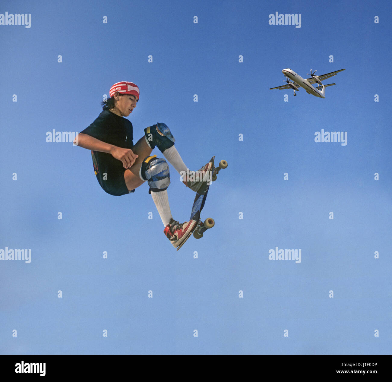 A young man skateboards in a skateboard park as a commerical aircraft flies over Stock Photo
