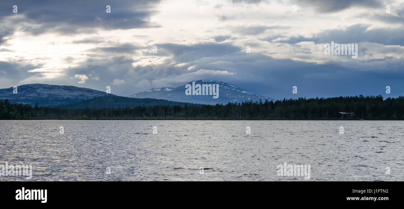 Subalpine lake against forest and mountain peaks with cloudy sky Stock Photo