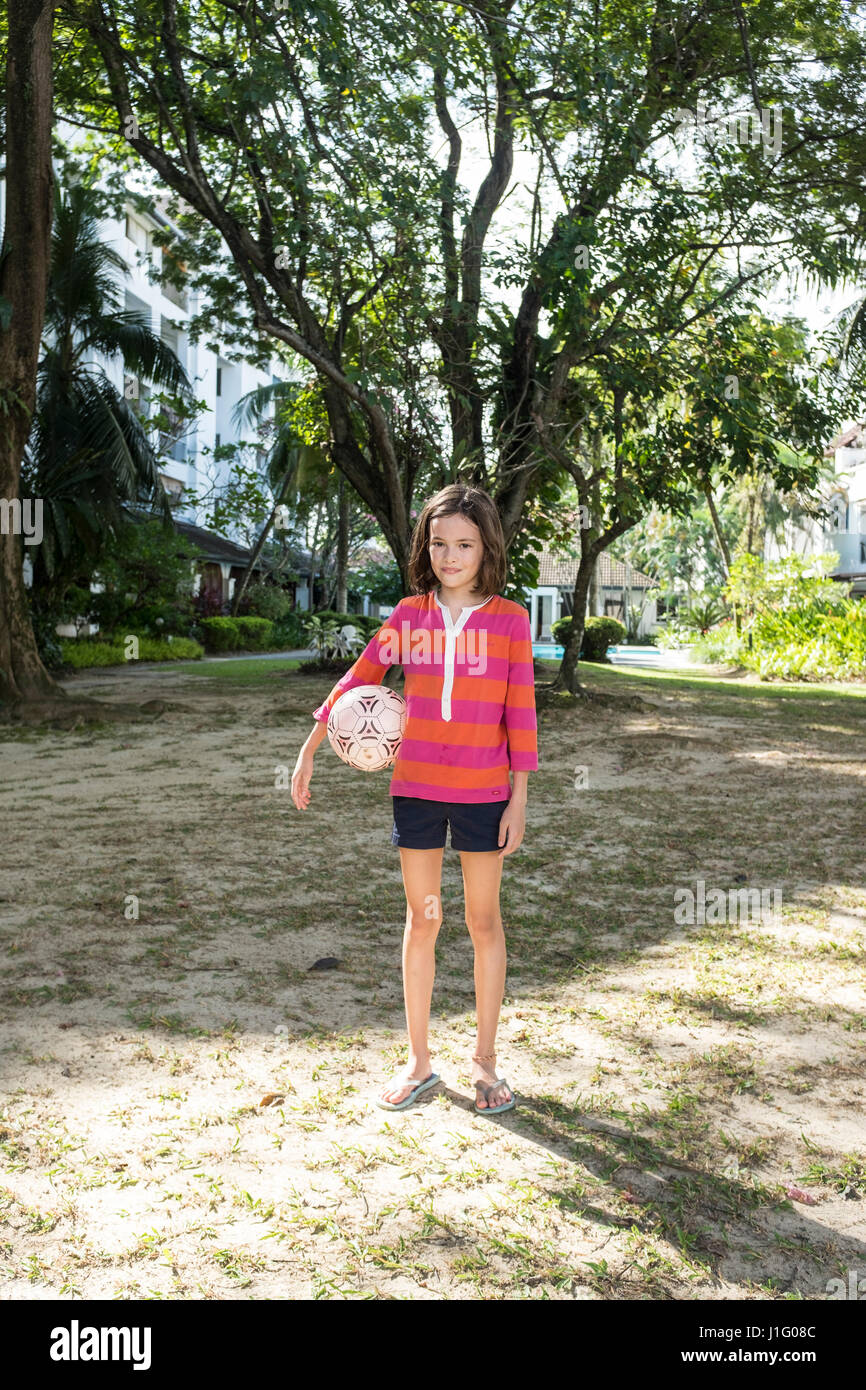 A 10 year old girl holds a football in a small park Stock Photo