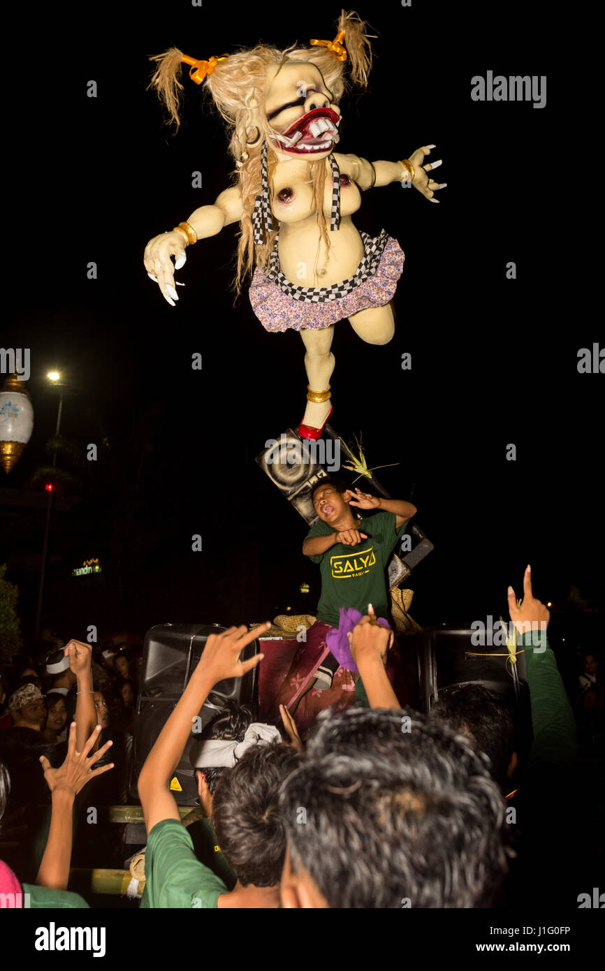 Balinese guy beneath scary Ogoh-Ogoh statue dancing to the music with the crowd of spectators loving every minute of it during Balinese New Years Eve Stock Photo