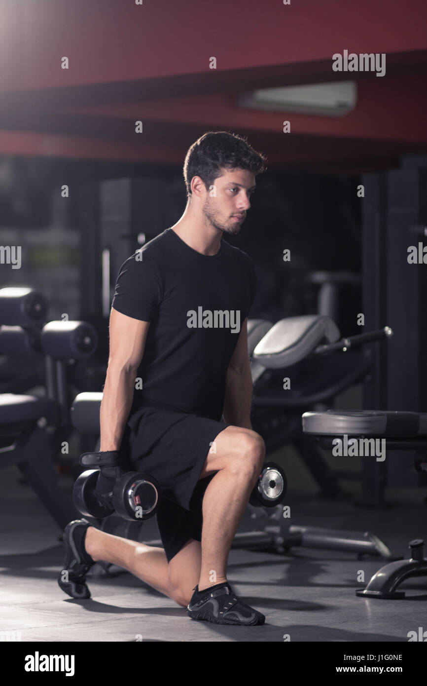 young man exercise dumbells leg squat, indoors gym. Stock Photo