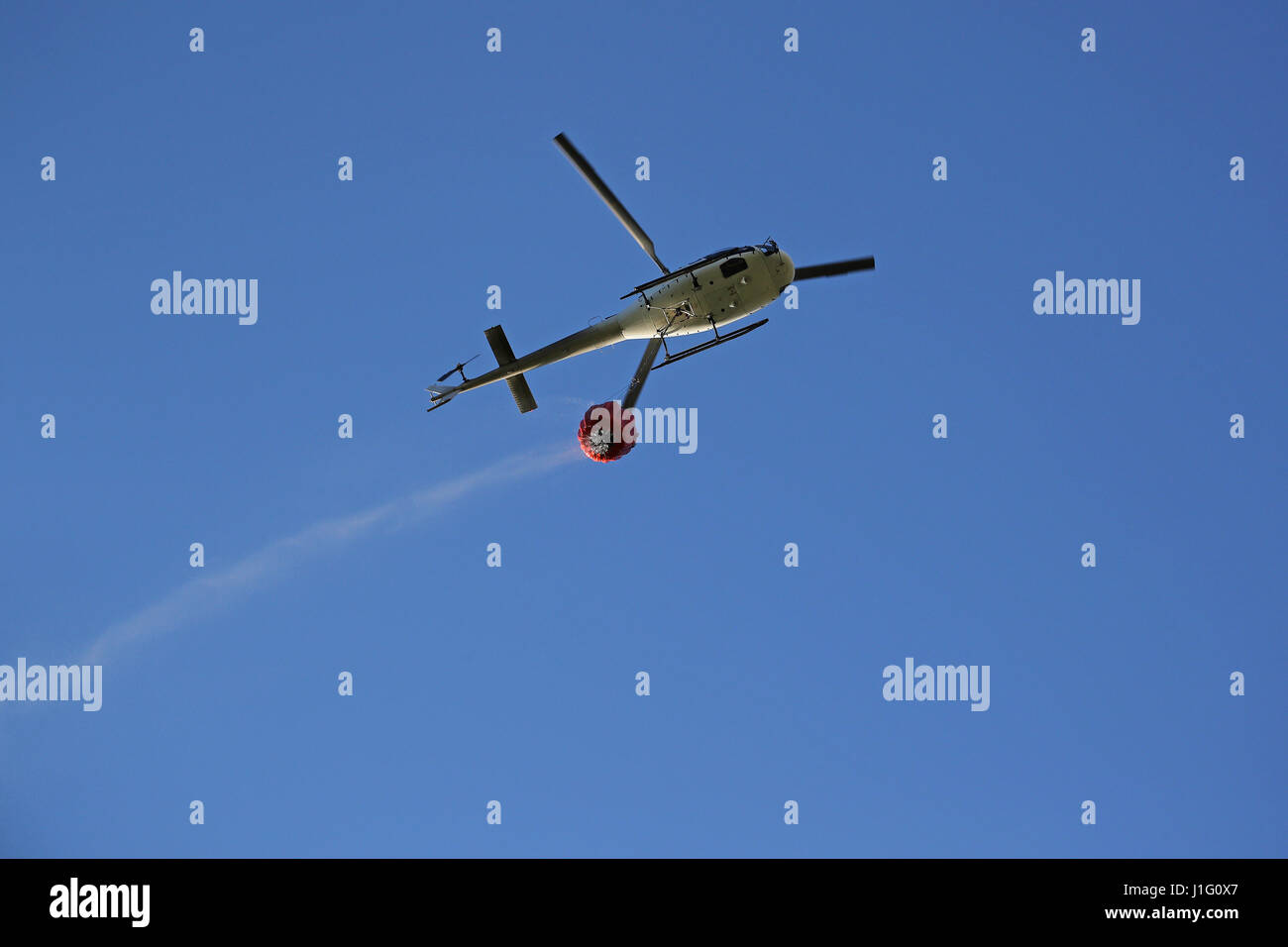 Firefighting helicopter with water bucket and trail of drops seen from