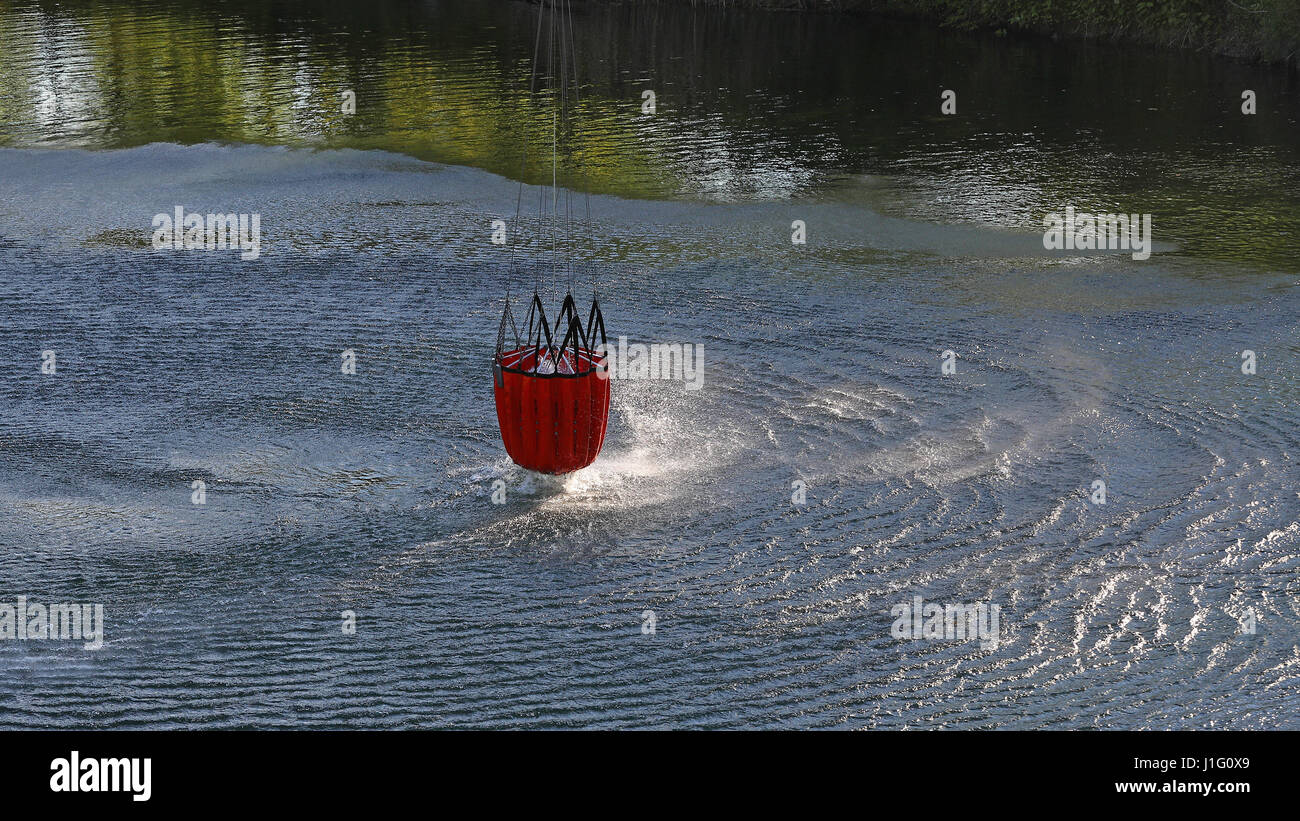 Detail of water bucket lifting out of the water under a helicopter with rotor wash on the surface of the lake Stock Photo