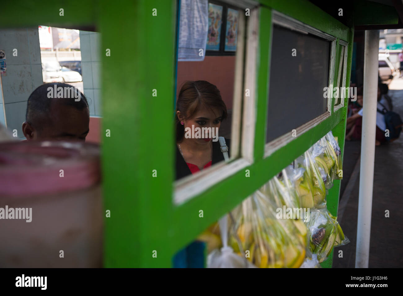 27.01.2017, Yangon, Republic of the Union of Myanmar, Asia - A woman is reflected in a mirror of a stall for mangos at the roadside. Stock Photo