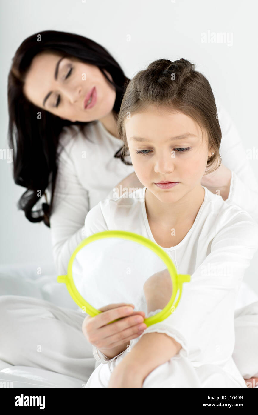 Smiling mother combing hair of cute little daughter with hand mirror Stock Photo