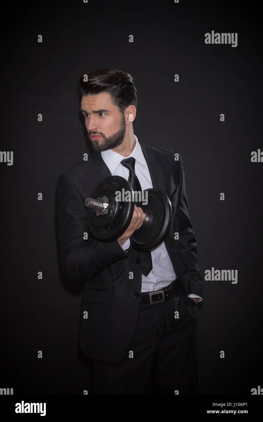 one young handsome man fitness dumbbell exercise, black background, elegant suit tie shirt pants jacket Stock Photo