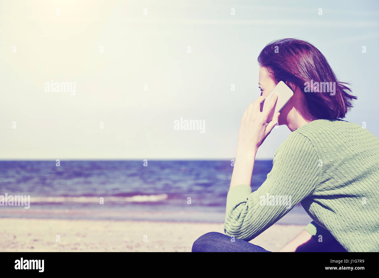 Vintage toned picture of a woman talking on a mobile phone on a beach, side view with copy space. Stock Photo