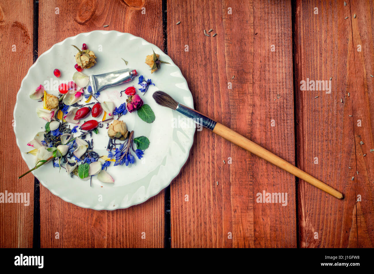 Art conceptual photo with flowers, brush, tube with paint on a plate on a wooden background Stock Photo