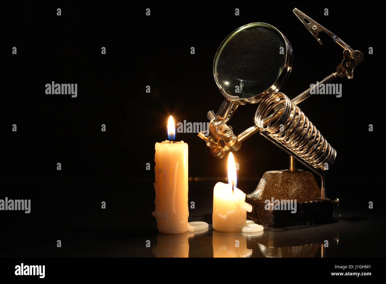 Retro laboratory equipment with magnifying glass near lighting candles on dark background Stock Photo