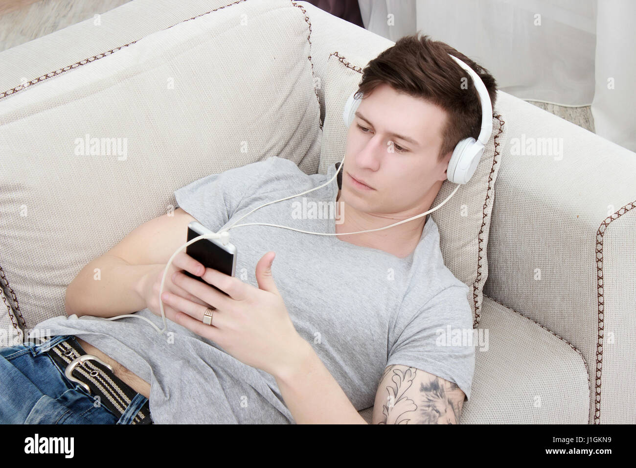 man listening to music with headphones and smartphone while relaxing on sofa Stock Photo