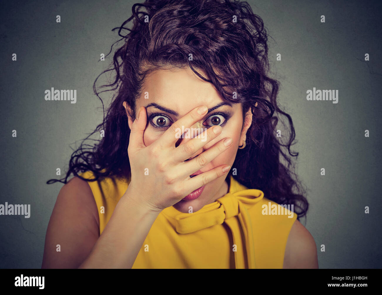 Scared young woman covering her face with hands peeking through fingers Stock Photo